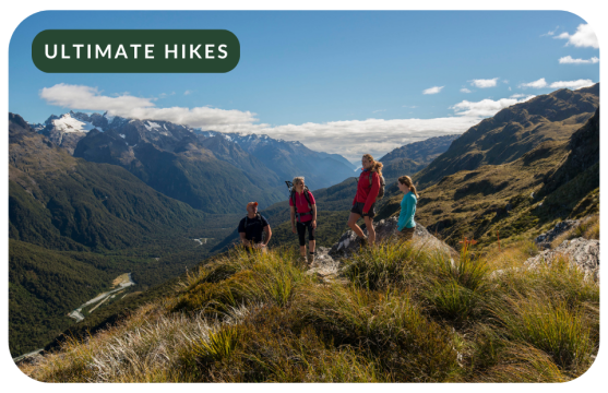 Four hikers standing on a mountaintop on the Routeburn Track, overlooking New Zealand?s mountains and valleys