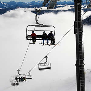 A chairlift comes through the thick white cloud with snowy mountain peaks in the horizon