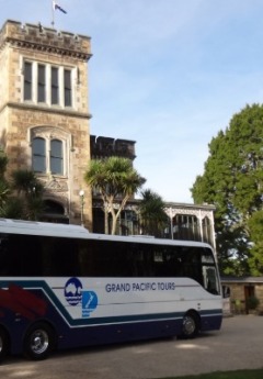 A Grand Pacific Tours bus is parked in front of a historic castle-like building.