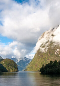 Green mountains surround calm water under a cloudy sky