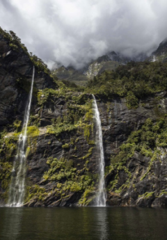 Twin waterfalls cascading down lush, rocky cliffs into a serene body of water.