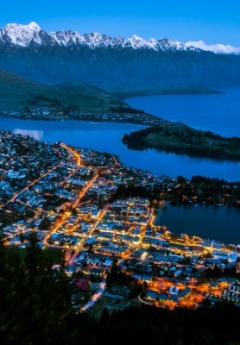 An aerial shot of Queenstown at dusk, with lights and snow-capped mountains.