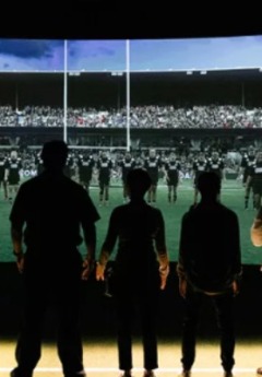 Silhouetted people watch a large screen showing a rugby game.