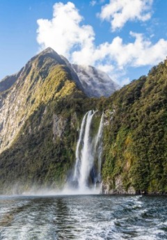 A boat's wake is seen as it cruises past a large waterfall.