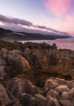 Pancake Rocks formations are silhouetted against a pastel-colored evening sky.