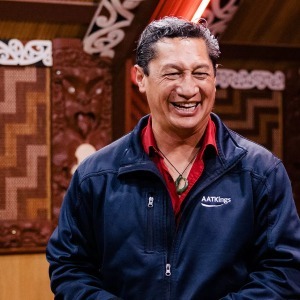 A smiling AAT Kings guide wearing a jade pendant inside a Maori meeting house.