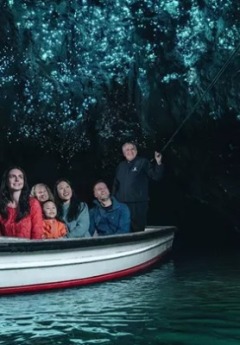 A guide poles a boat carrying tourists viewing glowworms on the ceiling of a dark cave.