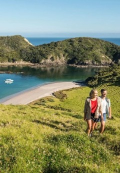 A couple smiles while hiking up a grassy hill overlooking a beautiful secluded bay.