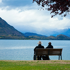 Two people take a rest on a bench overlooking Lake Wanaka, on an overcast day.