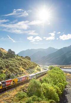 TranzAlpine train winding along riverbank in Southern Alps
