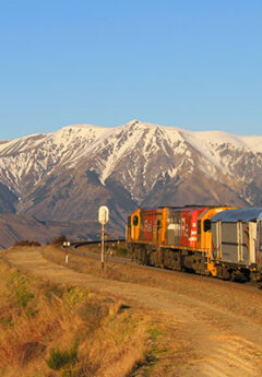 Tranzalpine train heading towards snow-capped mountains of Arthurs Pass