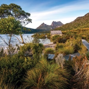 A wooden boardwalk leads toward a boatshed on Dove Lake with Cradle Mountain visible.