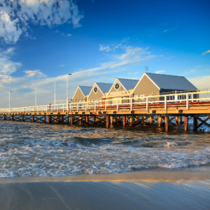 Waves rolling in on the beach with a long jetty and four buildings on the jetty