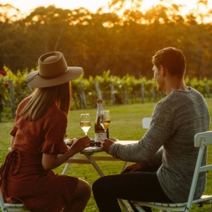 A couple enjoys a meal and drinks in a vineyard.