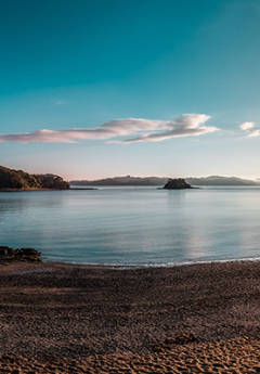 Paihia Beach at sunset with golden brown sand and still waters reflecting the sky