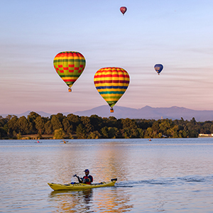Kayaker on Lake Burley-Griffin at sunrise and hot air balloons in the sky
