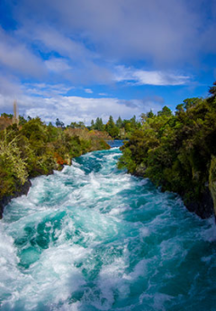 The turquoise water of the Huka Falls rushes rapidly through a narrow gorge.