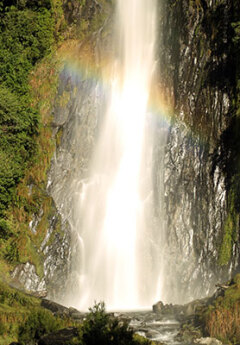 A rainbow forms on the Thnder Creek Falls in Haast Pass, New Zealand.