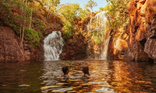 A couple swimming below twin waterfalls in a rocky gorge.