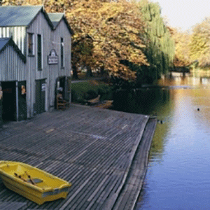 A dock leads down to the Avon river in Christchurch New Zealand, with a yellow boat on the dock near the boatshed.