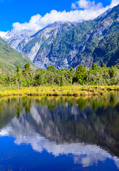 Mountains above a lake in Franz Josef and reflections in the lake