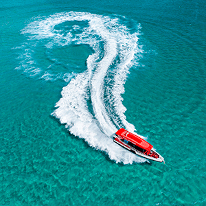 The bright red Rottnest Express boat creates whitewash in the crystal clear, turquoise waters surrounding the island