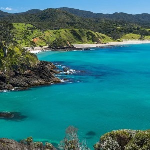 A beautiful bay with black rocks and turquoise water curves toward a white sand beach.