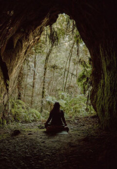 A person meditating inside a cave, surrounded by nature.