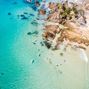 Aerial shot of crystal clear ocean water and coastline with surfers floating