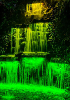 A waterfall glows green with artifical lights.