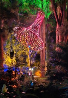 A large, funnel-shaped light sculpture hangs from the trees, glowing pink and red in the forest.