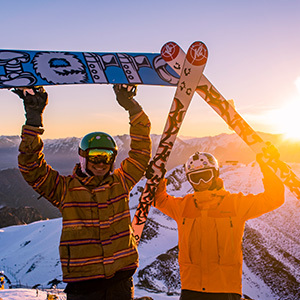 A skier and a snowboarder with planks in the air up Coronet Peak at sunset