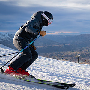 A person skiing down the white snow at Coronet Peak with the mountains in the background