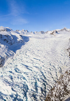 Blue skies contrast the white snow on Fox Glacier in winter