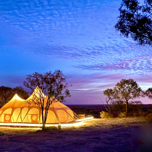 Illuminated tent at dusk with a backdrop of trees and a vibrant sunset.