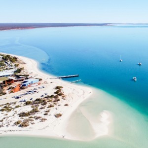 An aerial view of a white sand beach and town on a curving turquoise bay.