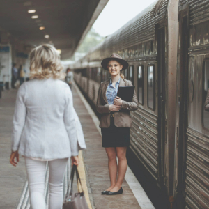 Host standing by the train with lady walking towards her