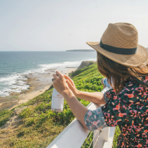 Lady standing with a Great Southern Drink bottle looking at the coastline