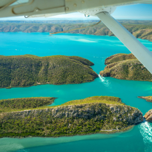 Plane wing with turquoise water below and rolling island hills