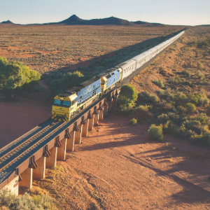 Train travelling through vast land with mountain in the back