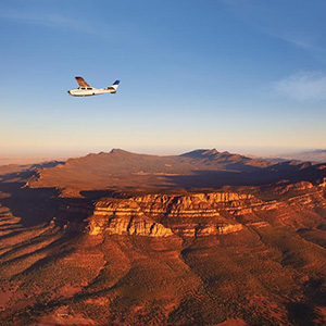 Small plane soaring above vast orange mountain ranges.