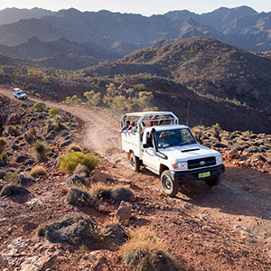 A rugged 4WD carrying passengers drives along a dusty mountain trail.