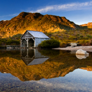 Wooden shelter on the lakefront with water reflecting the mountain background