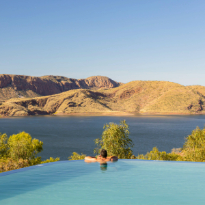 Infinity Pool with man in the centre looking at the large lake and large grassy hills