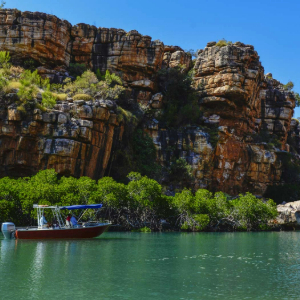 Boat travelling in water with red tall cliffs in the back