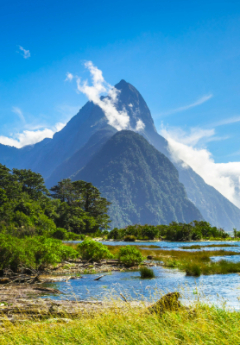 Multiple tall mountains in the back with a shrubs water in front