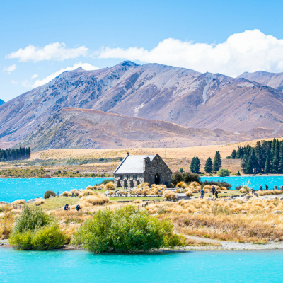 Mountains in the back with a blue lake and church in the centre with people surrounding