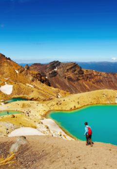 Man walking down a steep sloop with a red backpack and a volcanic terrain with deep blue tarns