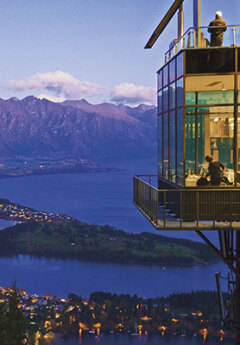 A scenic view of a city, lake, and mountains from the Skyline building at dusk.