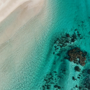Birds eye view of crystal clear water with dark reef with white sandy beach visible